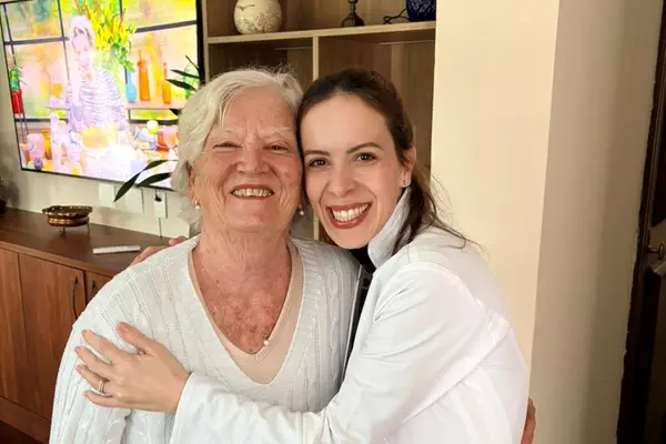Profissional sorrindo e abraçando uma idosa em ambiente acolhedor