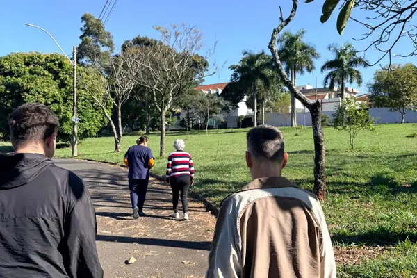 Idosos participando de caminhada ao ar livre com acompanhamento em área arborizada